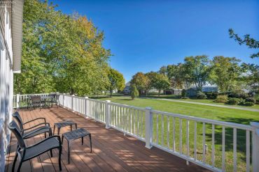 Sunny backyard deck with chairs and table overlooking green lawn and trees.