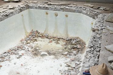 An empty, damaged pool with broken tiles and debris scattered inside.