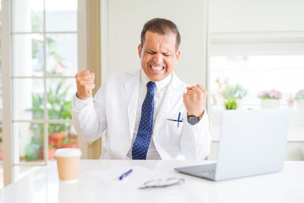 Image of a Medical Practitioner, with an excited expression in front of a laptop.