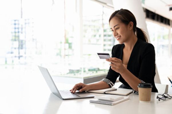 Image of a woman looking at a credit card while in front of her laptop computer.