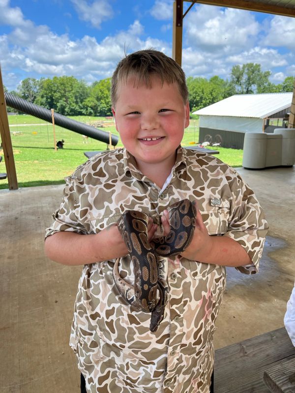 A smiling boy holding a brown and black snake outdoors.