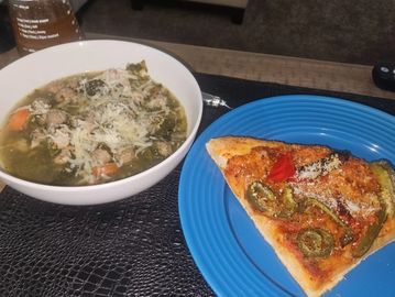 A bowl of soup and a slice of pizza on a table.