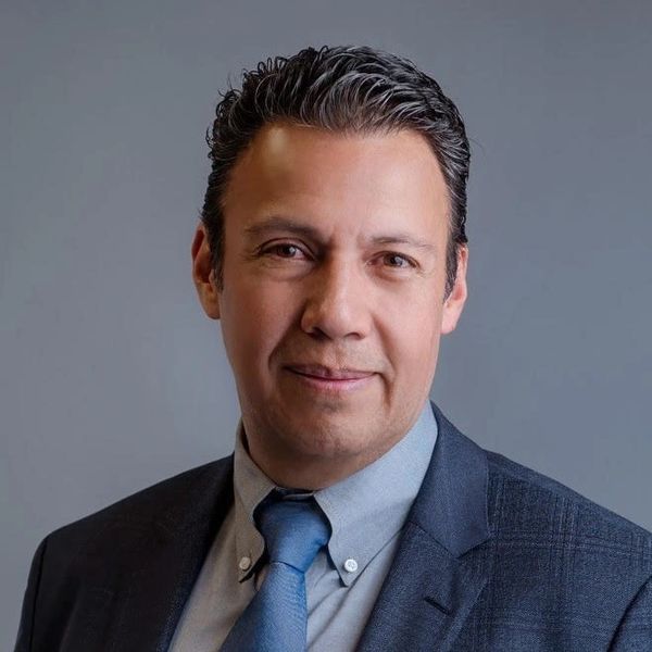 Professional man in a suit and blue tie against a gray background.