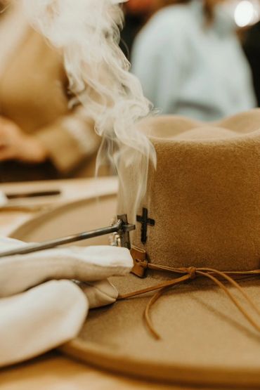 Branding a felt hat with a hot branding iron shaped like a cross causing smoke.