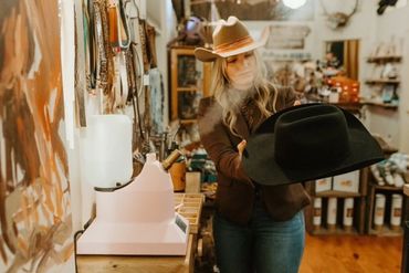 Woman steaming a western style felt hat to give it a new shape.