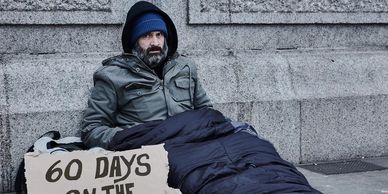 Homeless man sitting on the street with a sign.