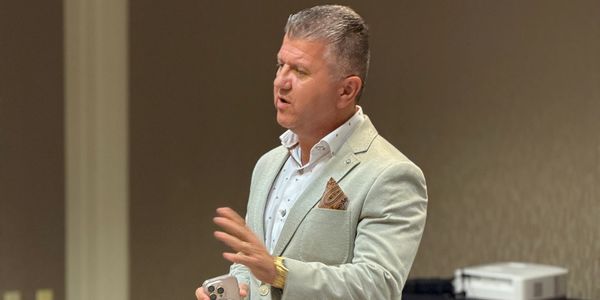Man in a light suit giving a presentation to an audience.