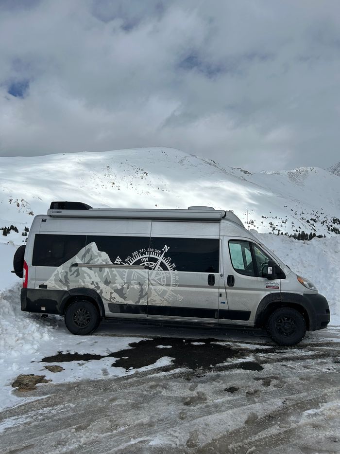 A camper van with mountain and compass design parked in snowy mountains.