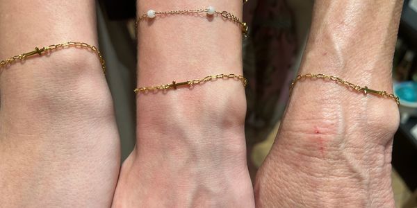 Three wrists wearing delicate gold chain bracelets with small cross charms.