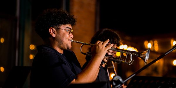 Musician playing trumpet in a dimly lit setting with warm lights.