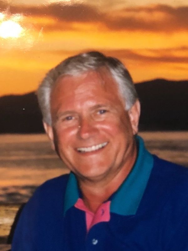 Smiling man with silver hair against a sunset backdrop by the water.