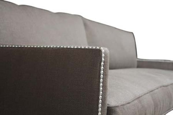 A modern grey sofa with nailhead trim detailing.