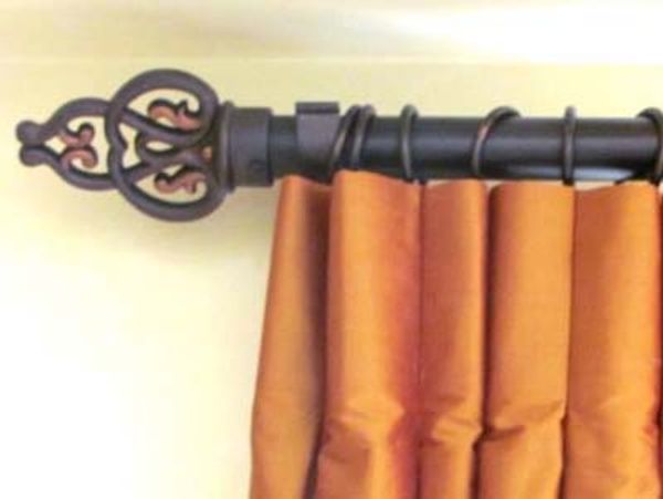 A decorative curtain rod with an ornate finial and golden drapes.