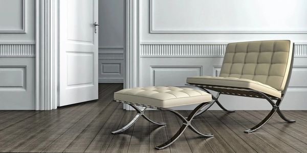 Modern white chair and ottoman in a minimalist room with an open door.