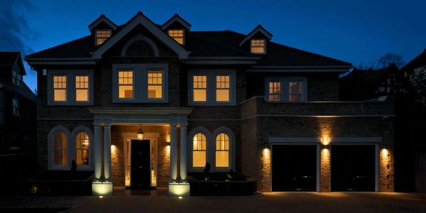 Elegant house warmly lit at night with multiple windows and a double garage.