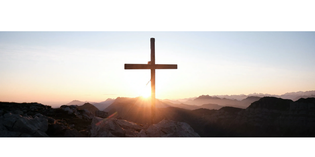 A cross on a mountain top with a sunrise
