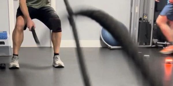 Man intensely working out with battle ropes in a gym.