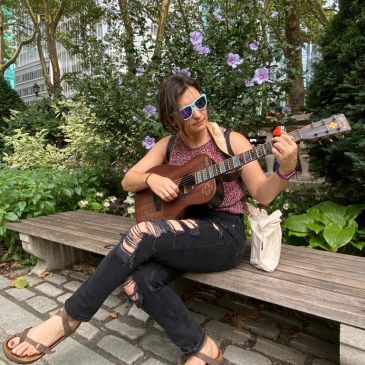 Person playing guitar on a bench in a park.