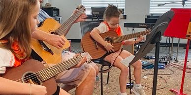 Children and adult playing guitar together indoors.