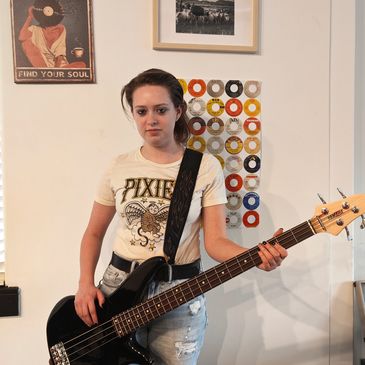 Young woman playing black bass guitar indoors.