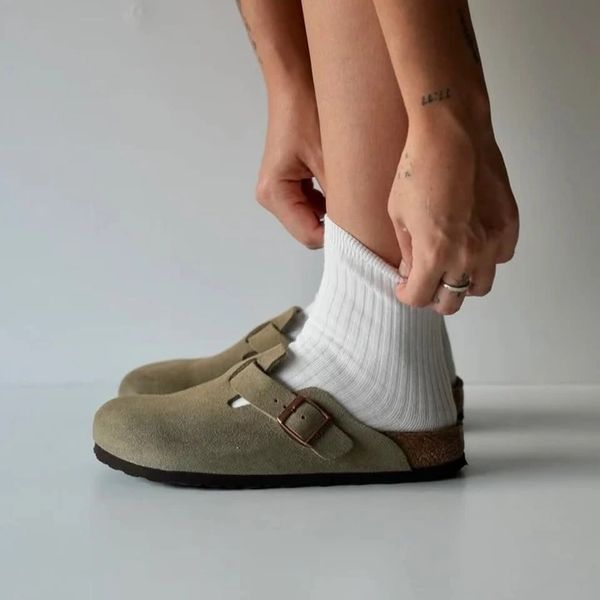 Person wearing beige slip-on clogs with white socks, adjusting sock.