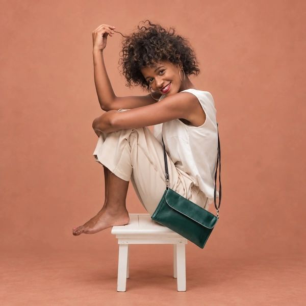 Woman sitting barefoot on a white stool with a green bag.