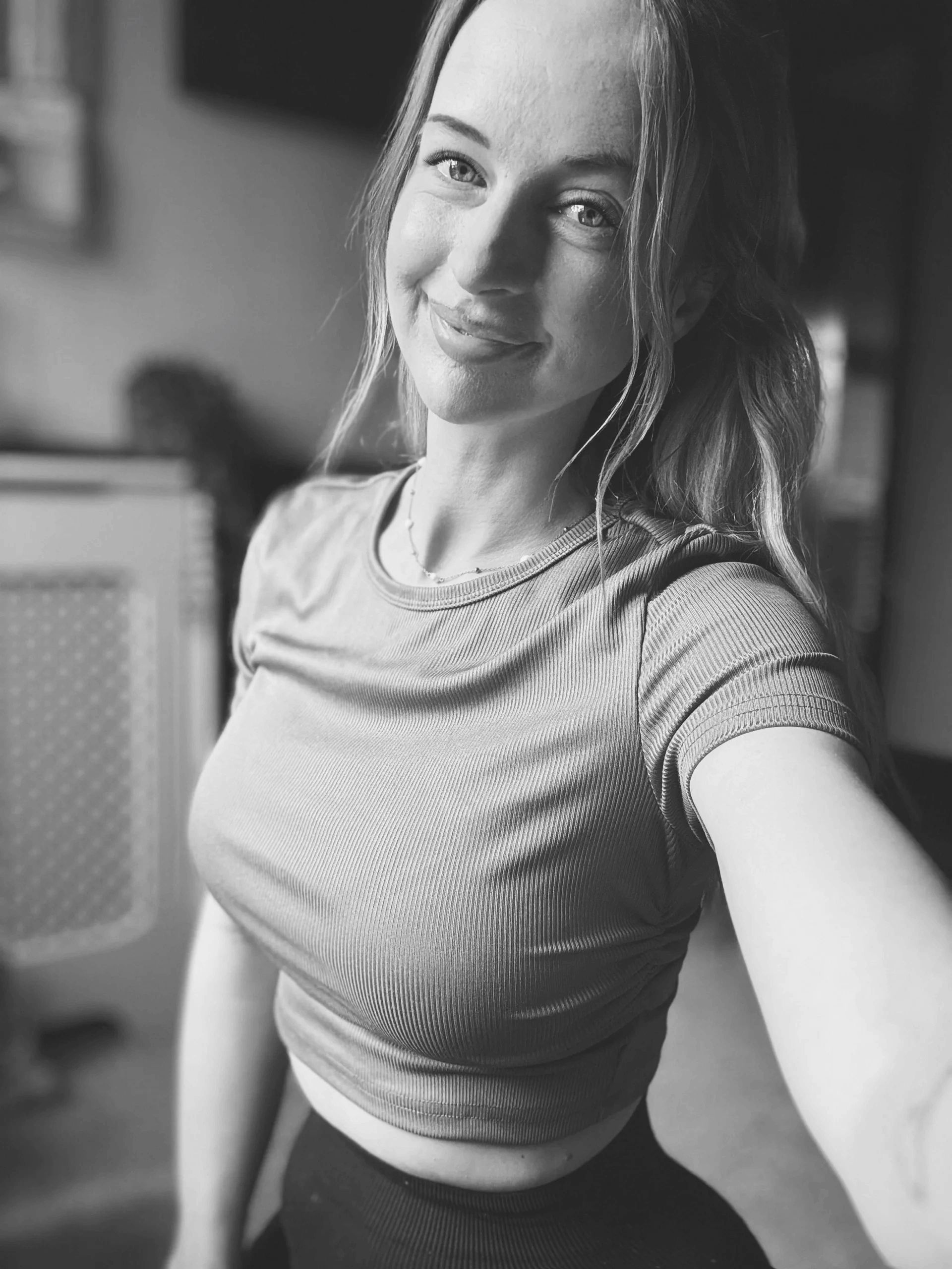 Black and white selfie of a smiling young woman wearing a crop top.