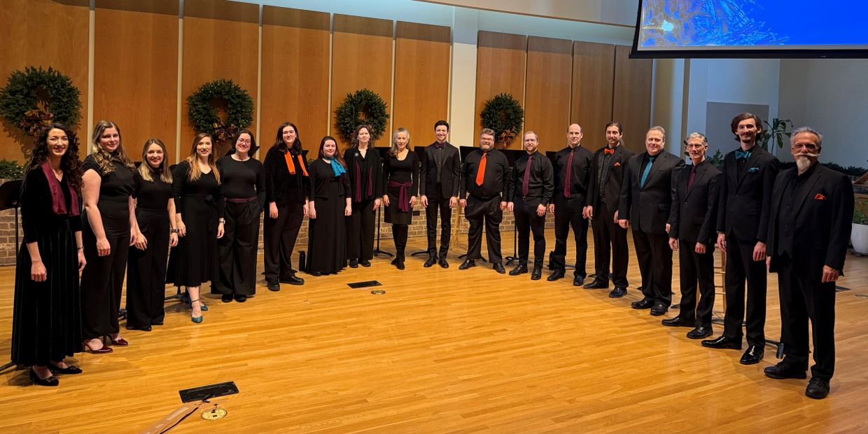 Choir group dressed in black with colorful accents standing in a semi-circle on stage.