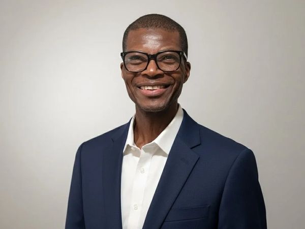 Confident man in glasses and navy blazer smiling warmly.
