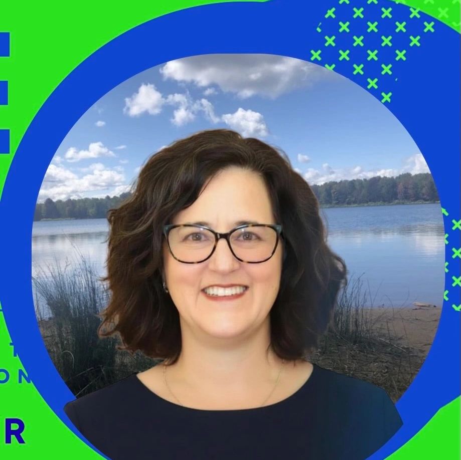 Smiling woman with glasses in front of a lake background.