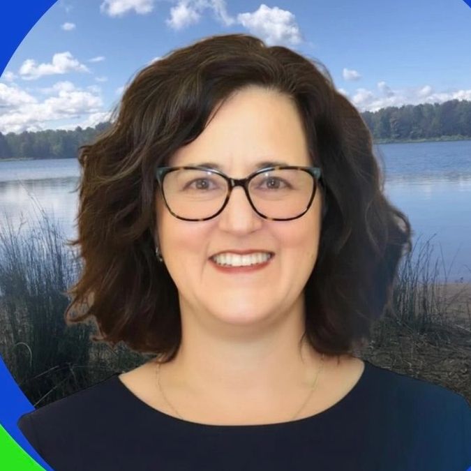 Smiling woman with glasses in front of a lake background.