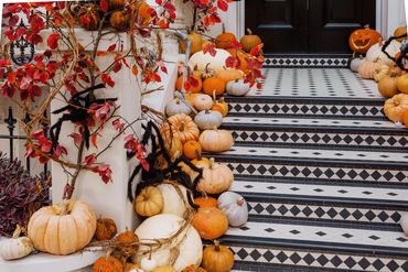 Halloween-themed porch decorated with pumpkins, autumn leaves, and large black spider decorations.