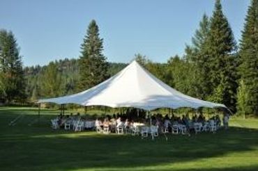 Outdoor event tent set up on a grassy lawn surrounded by trees.