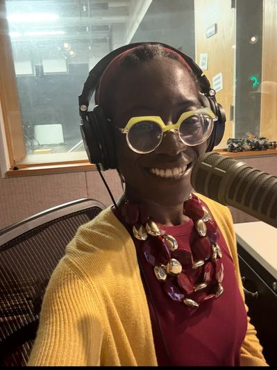 Smiling woman wearing headphones and glasses in a recording studio.
