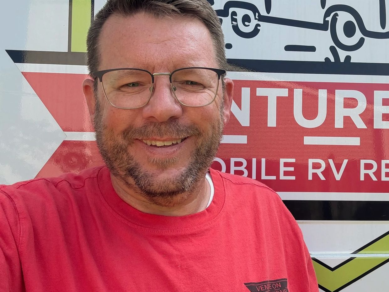 Man smiling in front of a red and white sign.