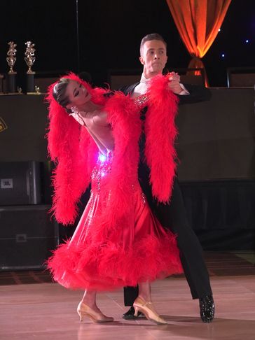 A professional ballroom dance couple from NIKA Dance in a tailsuit and red dress