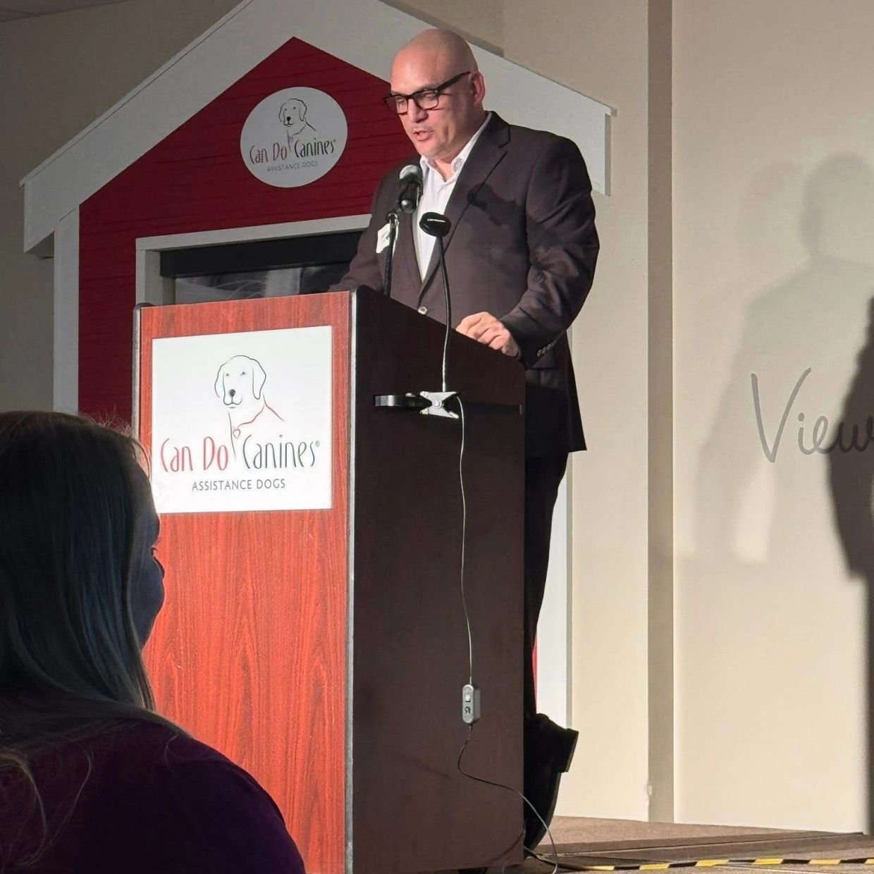 Man speaking at Can Do Canines event podium.