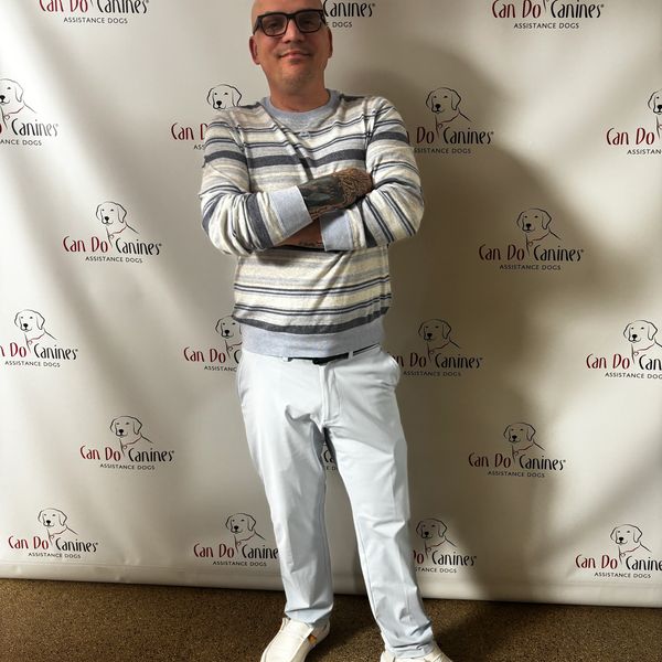 Man posing in front of a Can Do Canines backdrop.