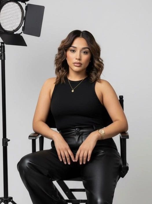 Confident woman sitting on a director's chair in stylish black outfit.