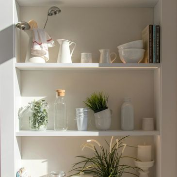 a picture of white shelves with organised jars, plates bottles and plants