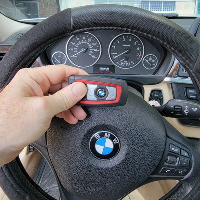 Hand holding BMW key fob inside a BMW car steering wheel.