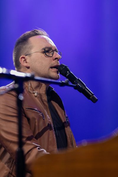 Male musician singing into microphone on stage.