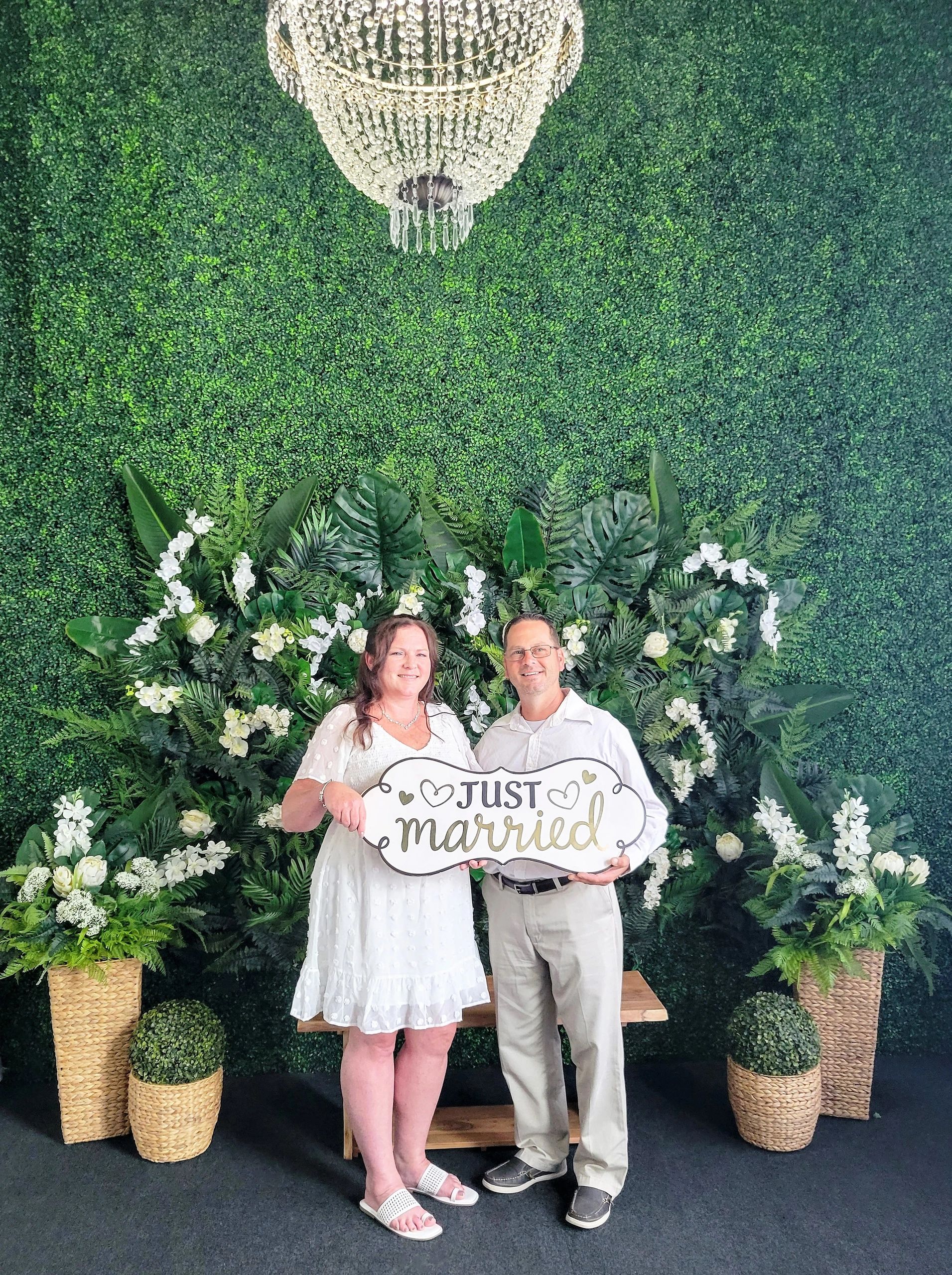 A smiling couple in the beautiful green indoor venue holding a sign saying, "Just Married."