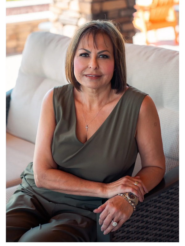 Woman in olive green outfit sitting on a couch with a calm expression.
