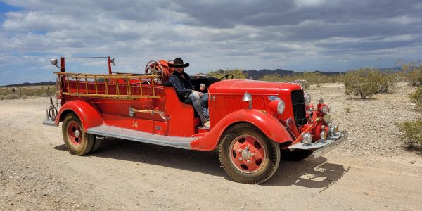 Man sitting on a vintage red fire truck in a desert.
