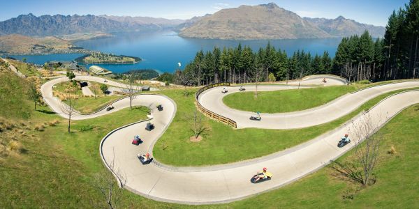 People riding go-karts on a winding track with a lake and mountains in the background.