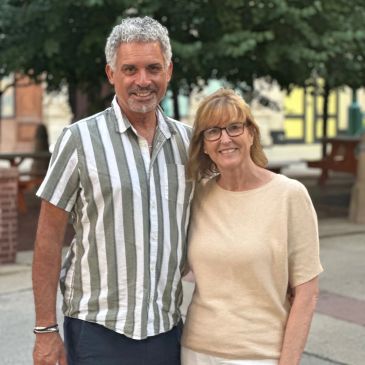 Smiling older couple outdoors with trees and benches.
