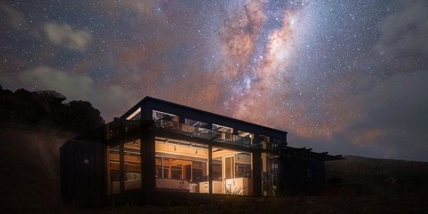 A modern house illuminated under a vibrant starry sky with the Milky Way.