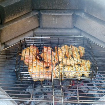 Chicken being grilled over charcoal in a wire basket.