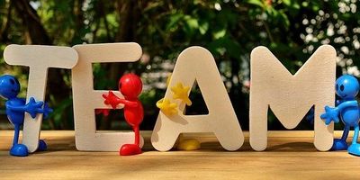 Wooden letters spelling T E A M with a greenery in the  background.
